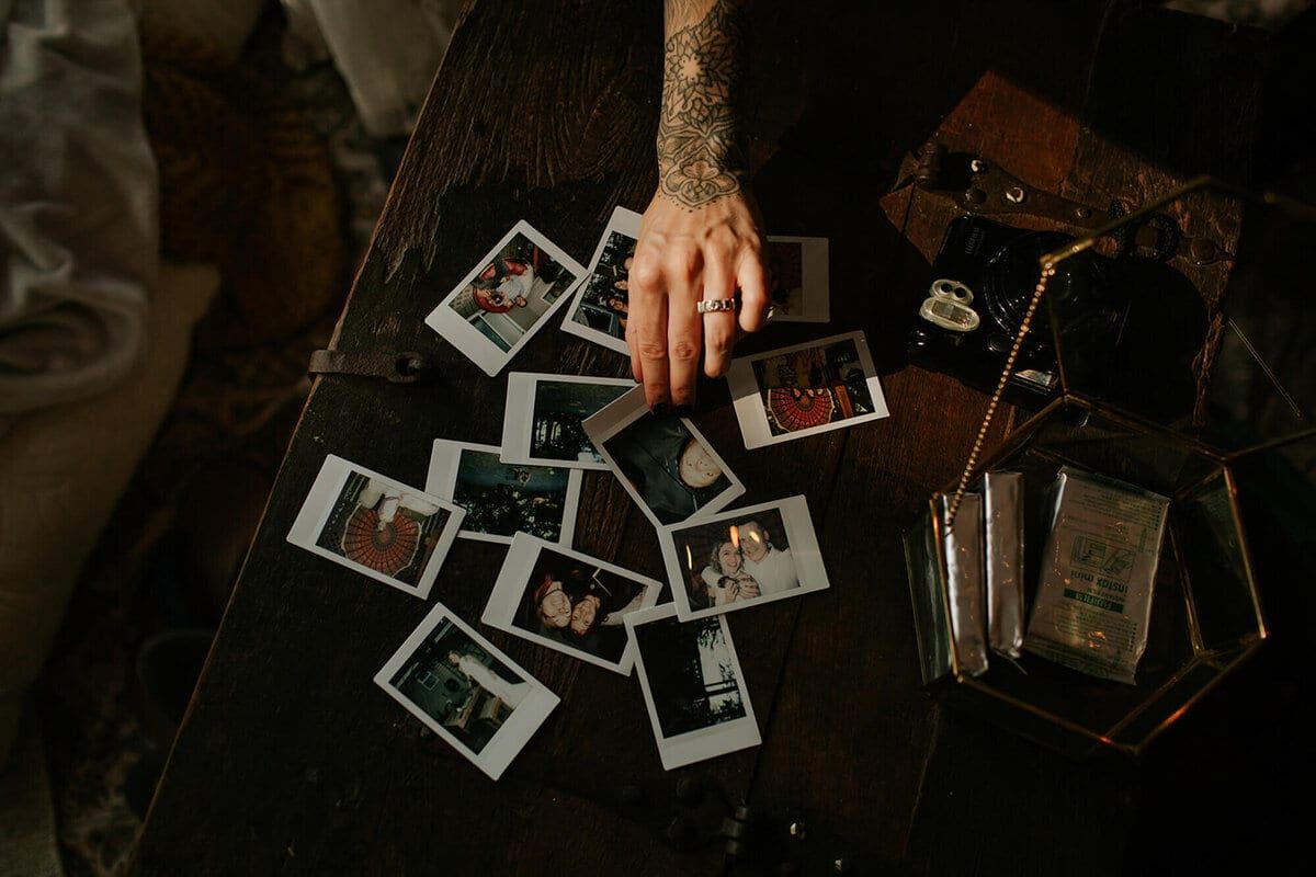 Tattooed hand arranging instant photos across a dark wooden table