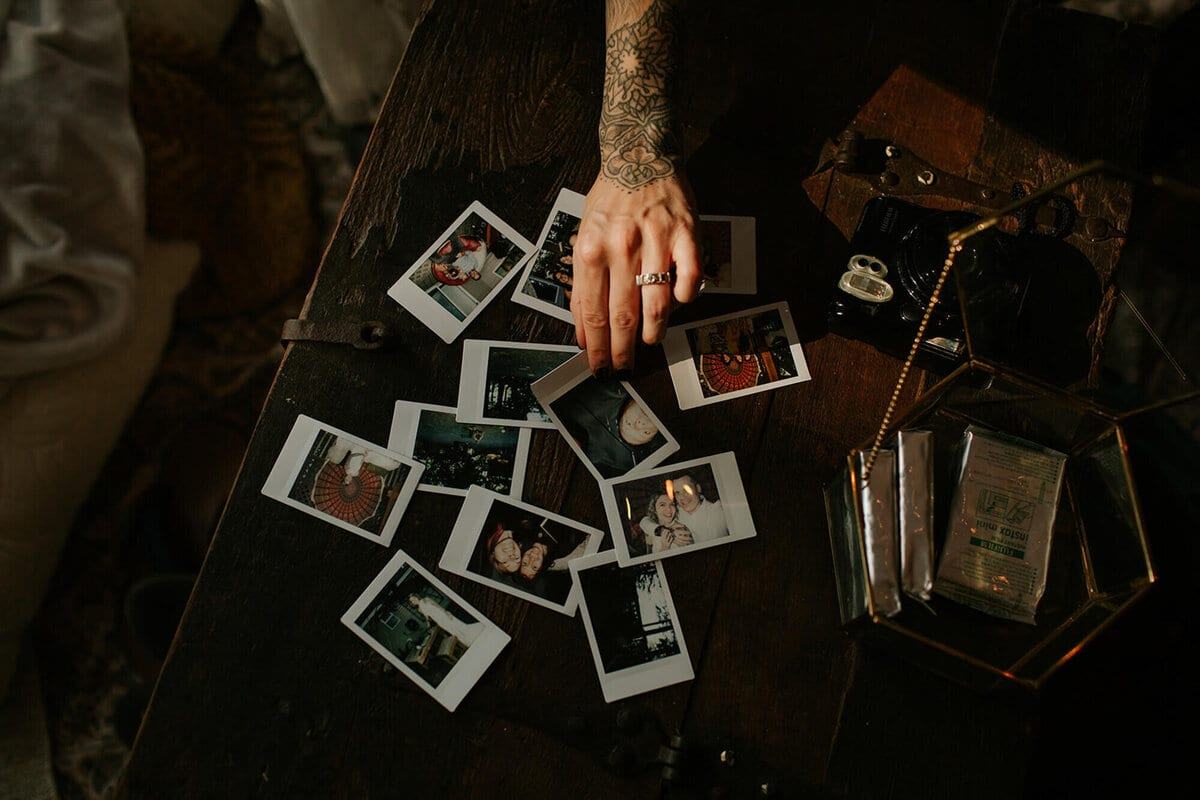 Tattooed hand arranging instant photos across a dark wooden table