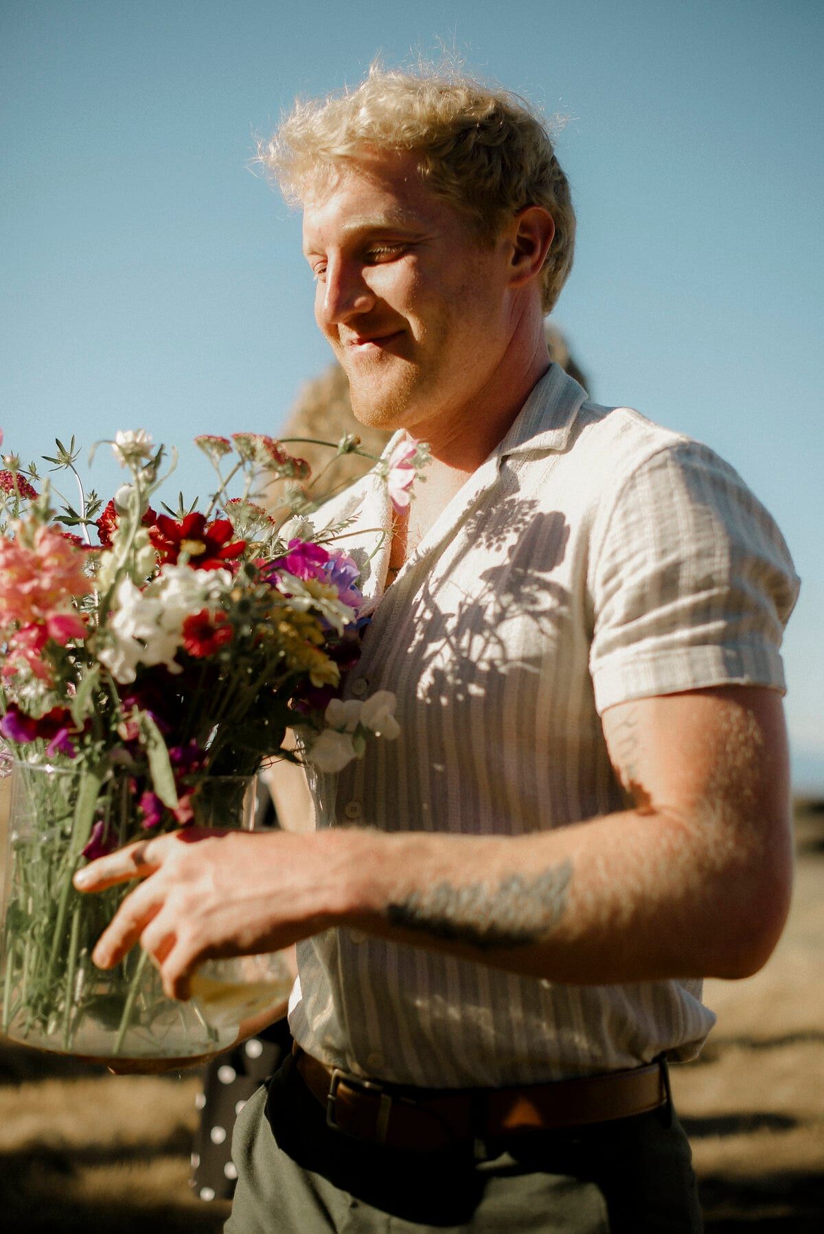 Blond man carrying a jar of wildflowers in golden sunshine