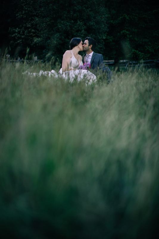 Newlyweds kissing while seated in deep meadow grass