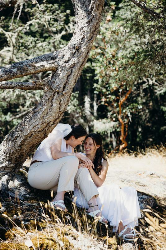 Two brides sharing a quiet moment beneath a leaning tree