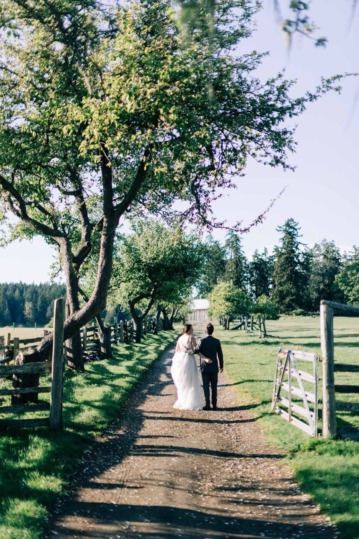 Couple strolling down a fenced dirt lane after the ceremony