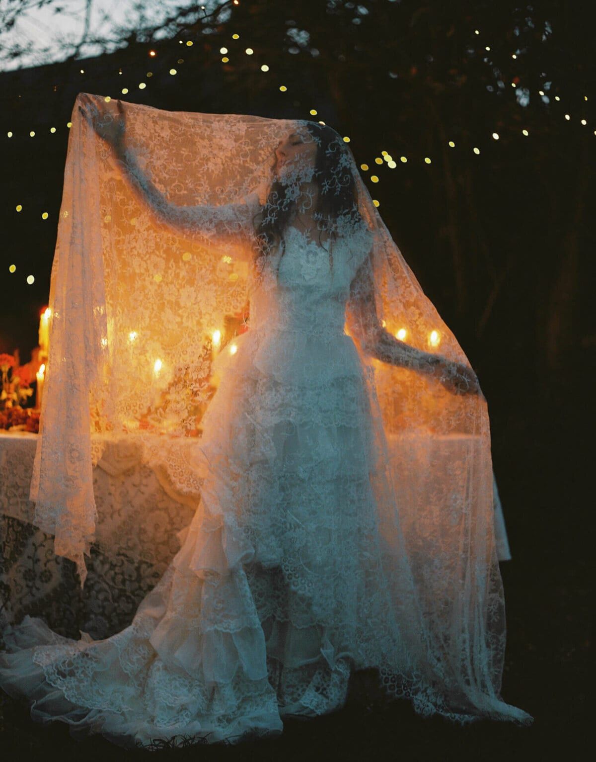 Lace-veiled bride at a candlelit table strung with fairy lights
