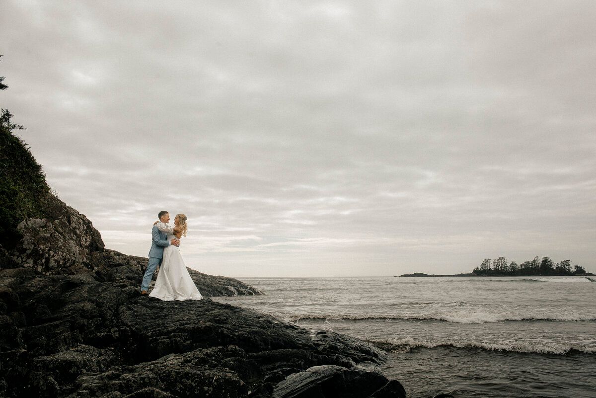 Couple standing together on ocean rocks with islands in the distance