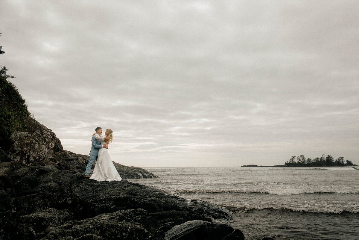 Couple standing together on ocean rocks with islands in the distance