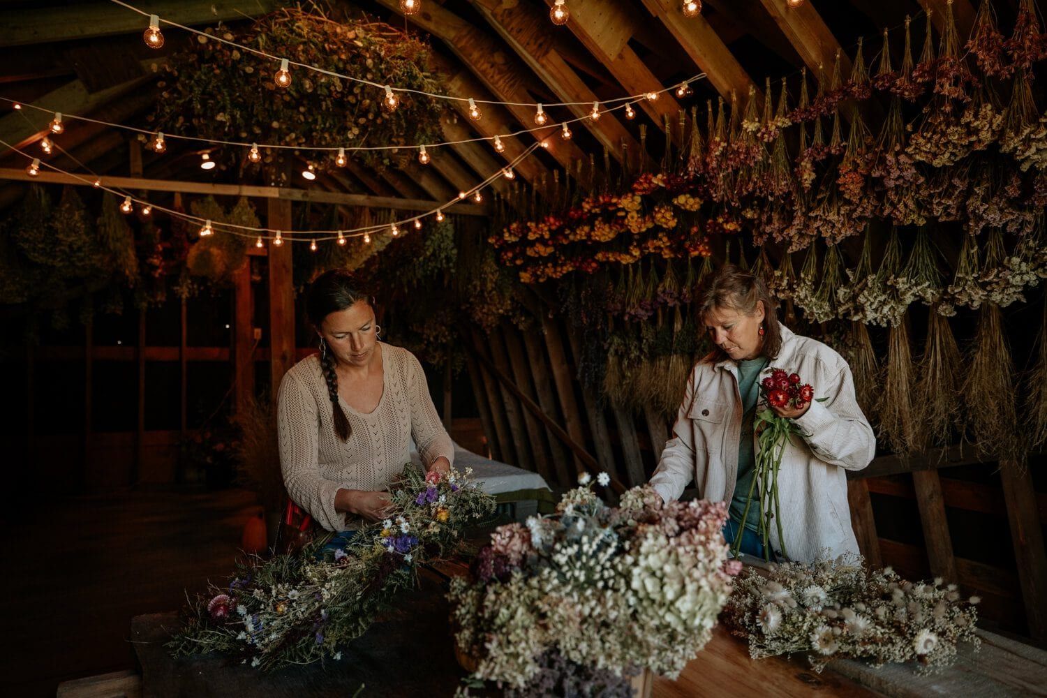 Two North Vancouver Island wedding florist arranging dried flowers in a rustic barn setting with hanging lights and floral displays