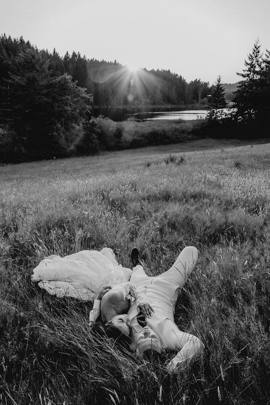 Newlyweds lying in tall meadow grass as sun sets over the lake