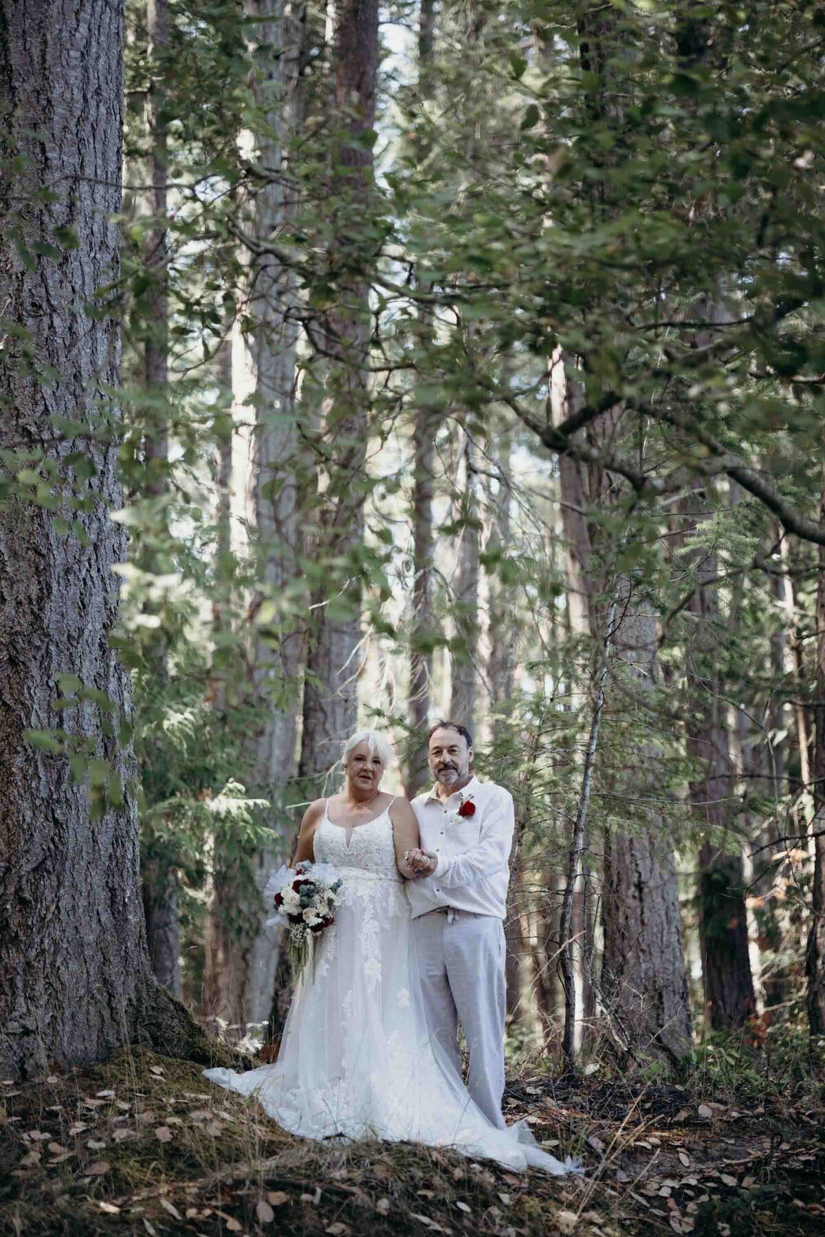 Older bride and groom dressed in white deep in the forest