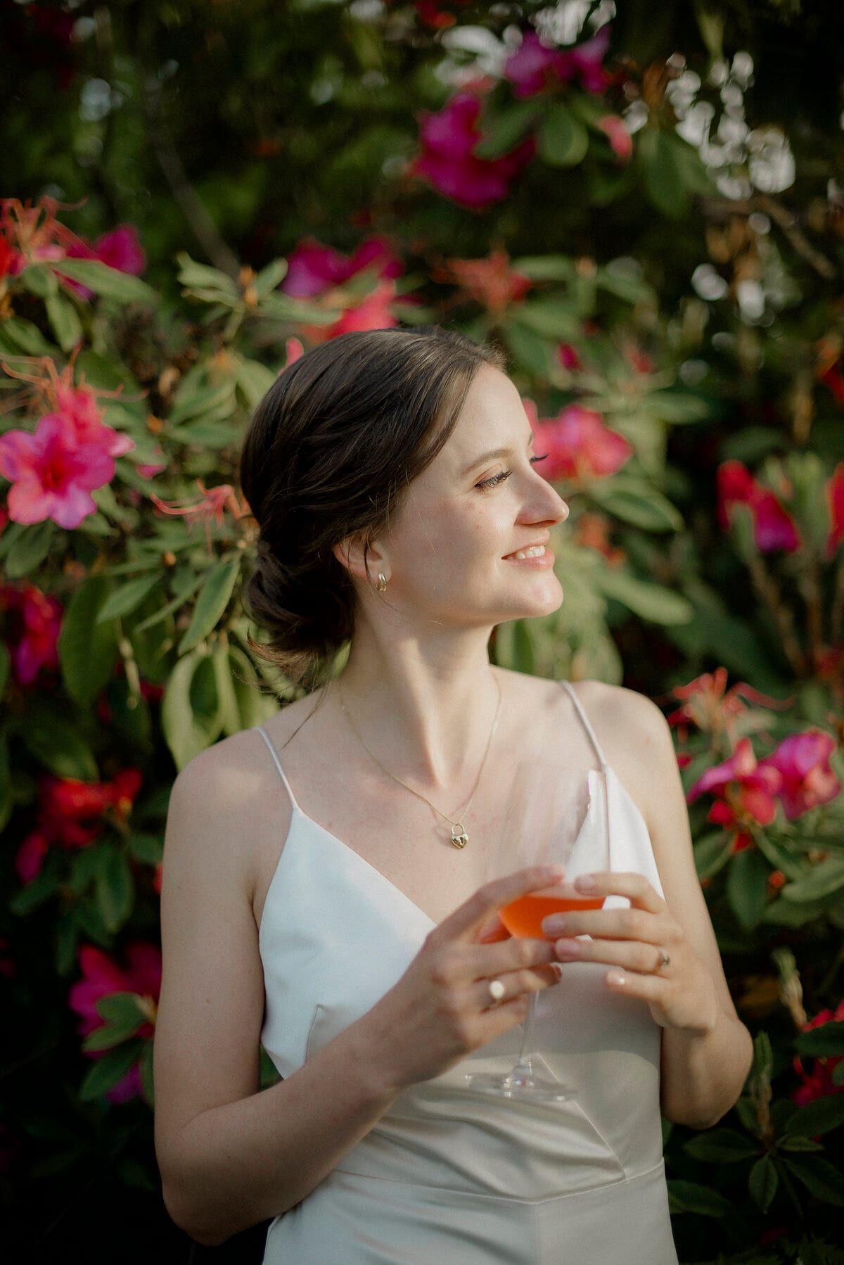 Bride with a cocktail smiling among pink rhododendron blossoms