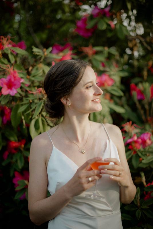 Bride with a cocktail smiling among pink rhododendron blossoms