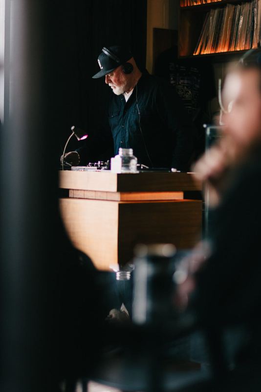 Bassos at the decks, framed by guests in a dim room