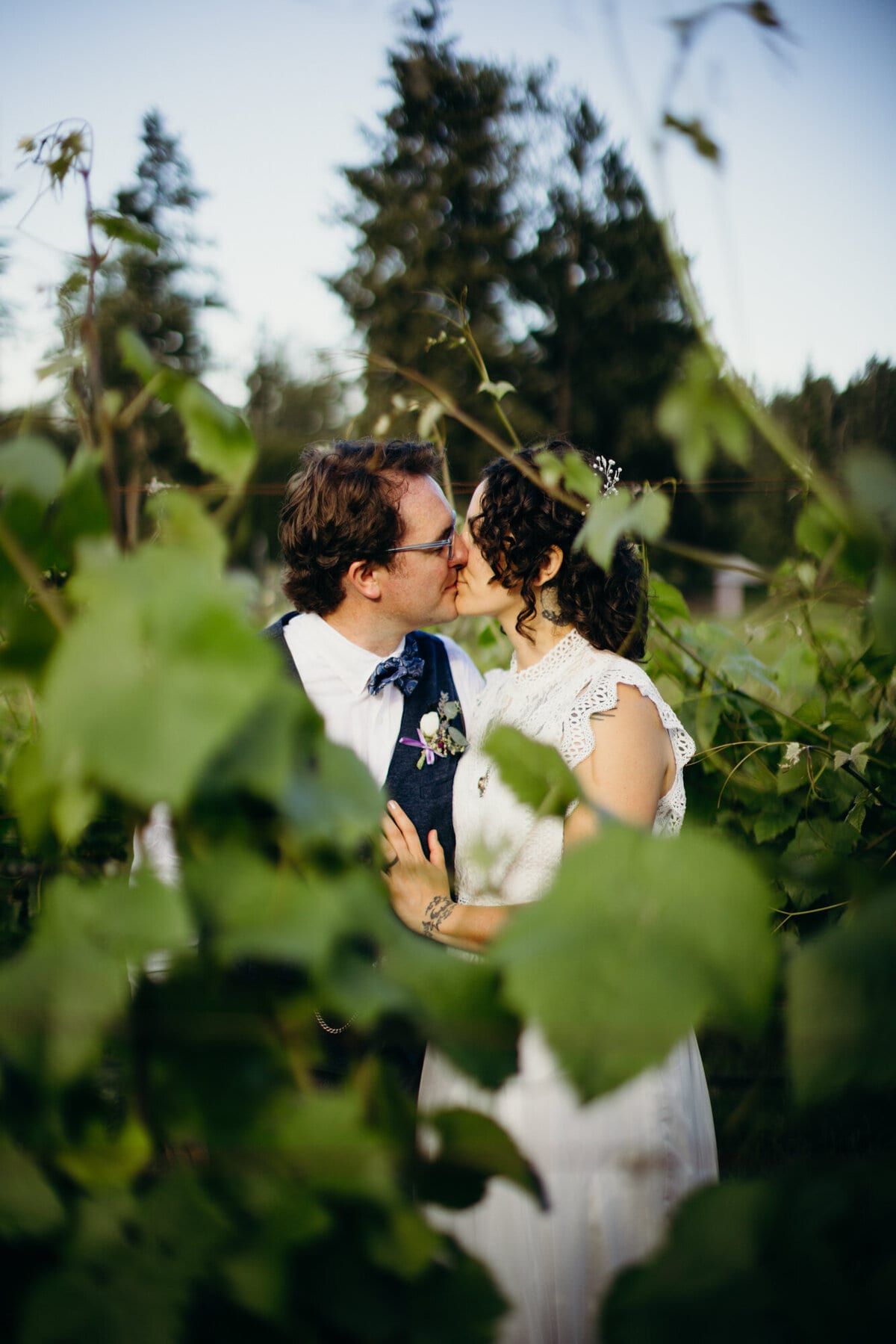 Bride and groom kissing amid sunlit grapevine leaves