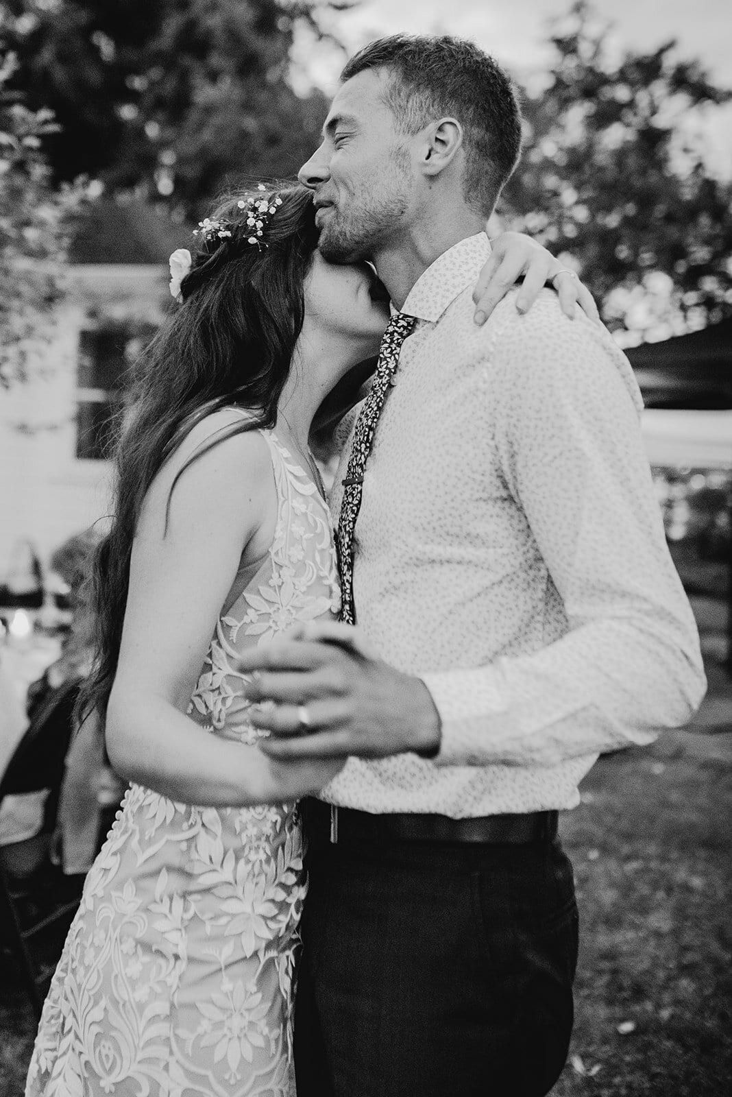 Bride kissing the groom's cheek during a backyard slow dance
