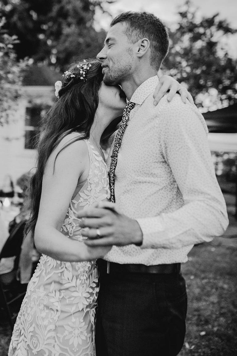 Bride kissing the groom's cheek during a backyard slow dance