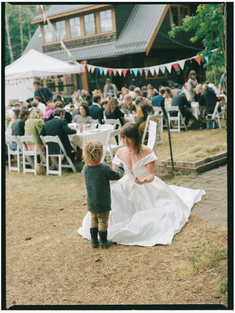 Bride crouching to chat with a small child at the outdoor reception