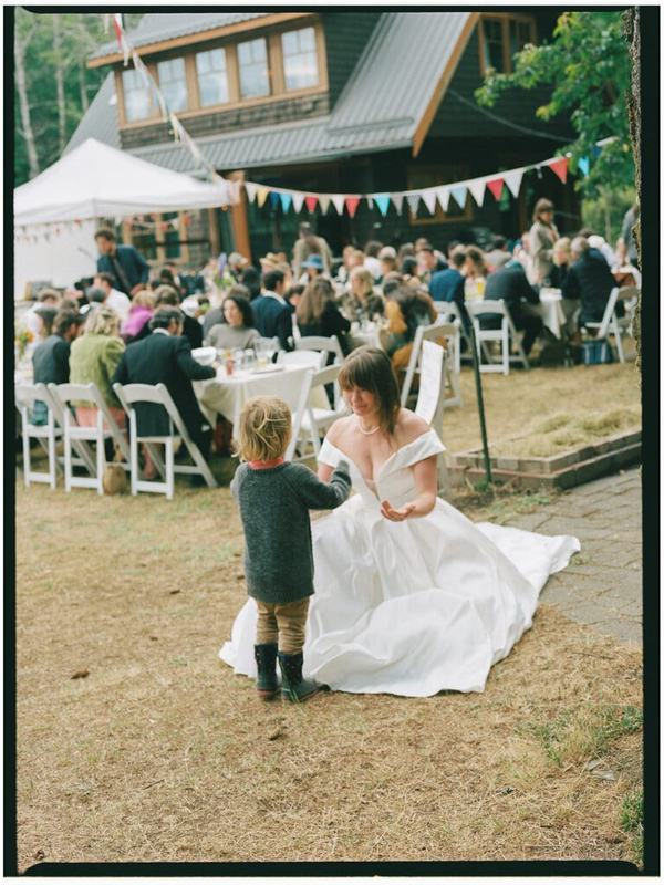 Bride crouching to chat with a small child at the outdoor reception