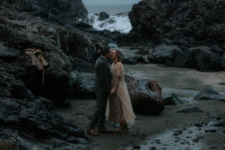 Windswept couple in blush and grey kissing on a stormy beach