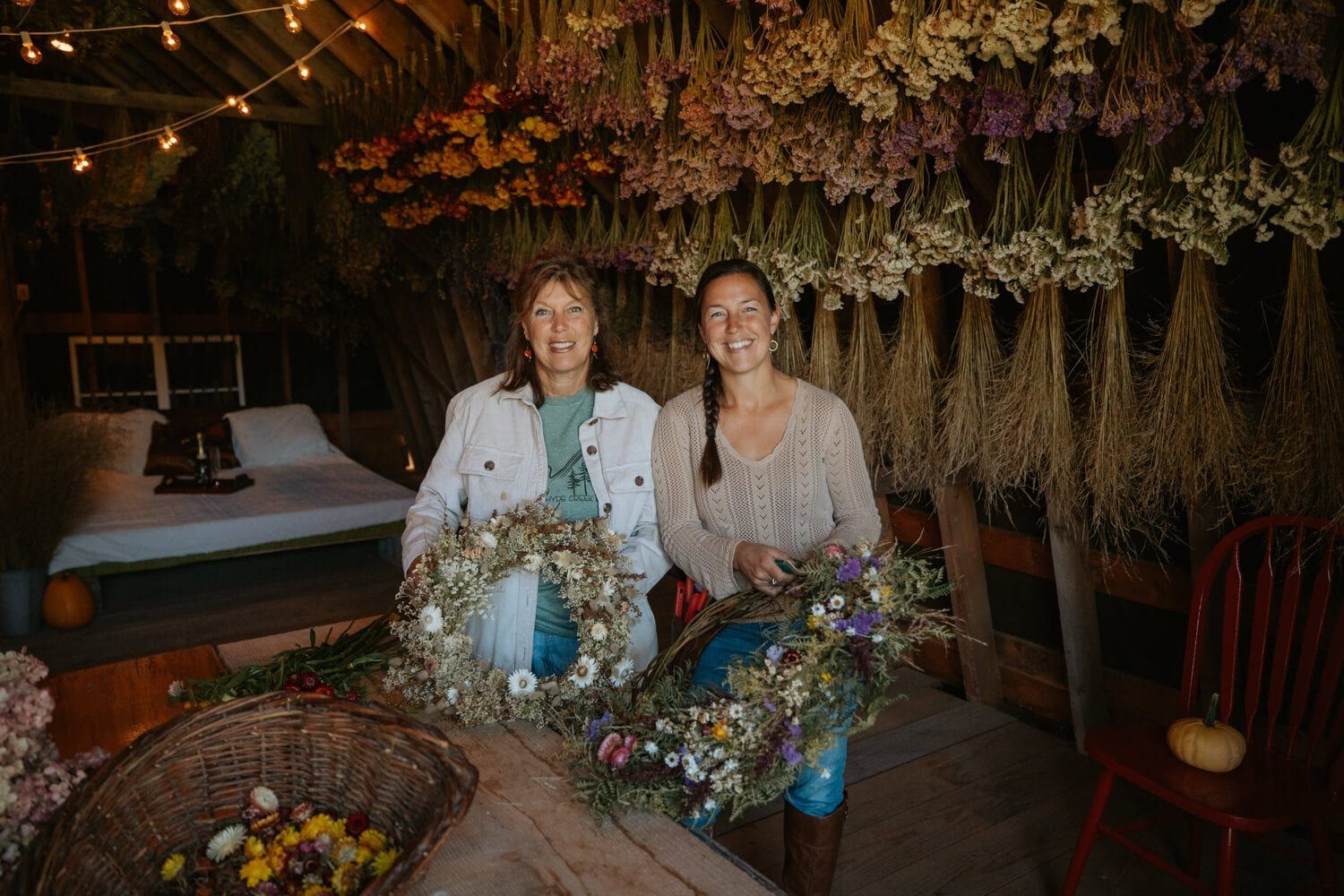Jenna and Georgia of Hyde Creek Flower Farm holding arrangements beneath hanging dried flowers