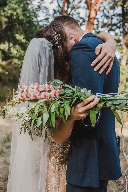 Bride hugging the groom's neck, snapdragon bouquet in hand