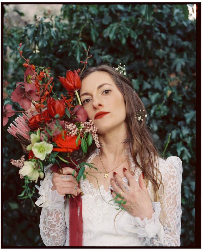 Bride with red lipstick holding a crimson bouquet against ivy