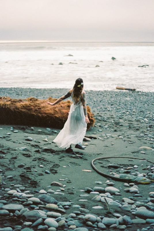 Bride crossing a rocky beach scattered with kelp and driftwood