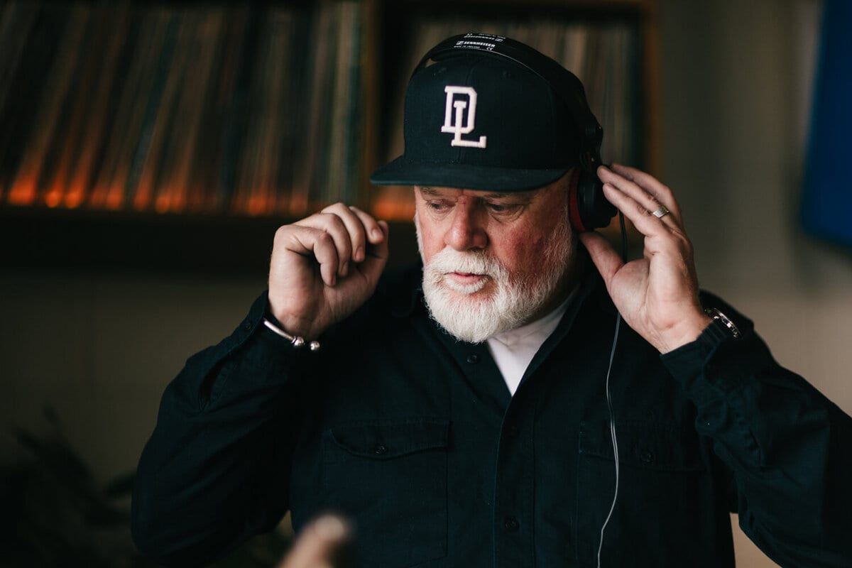 Headphones pressed to his ears in front of the record wall