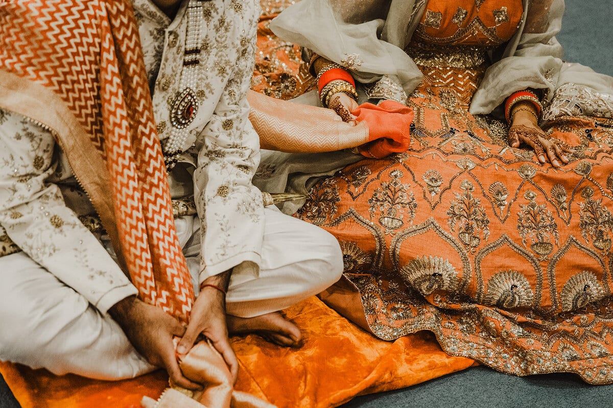 Embroidered orange and cream attire during a South Asian wedding ritual