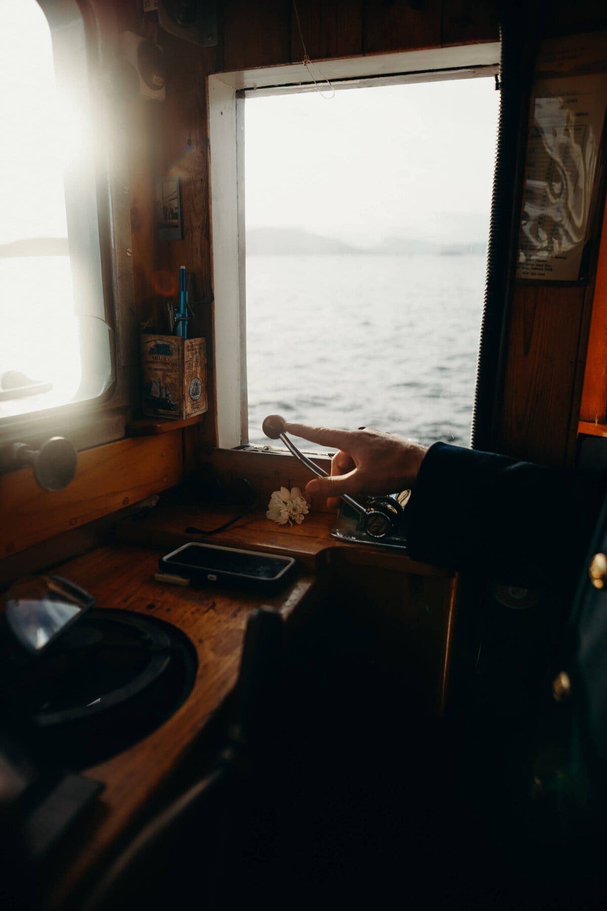 Hand resting on the controls inside the sunlit wooden wheelhouse