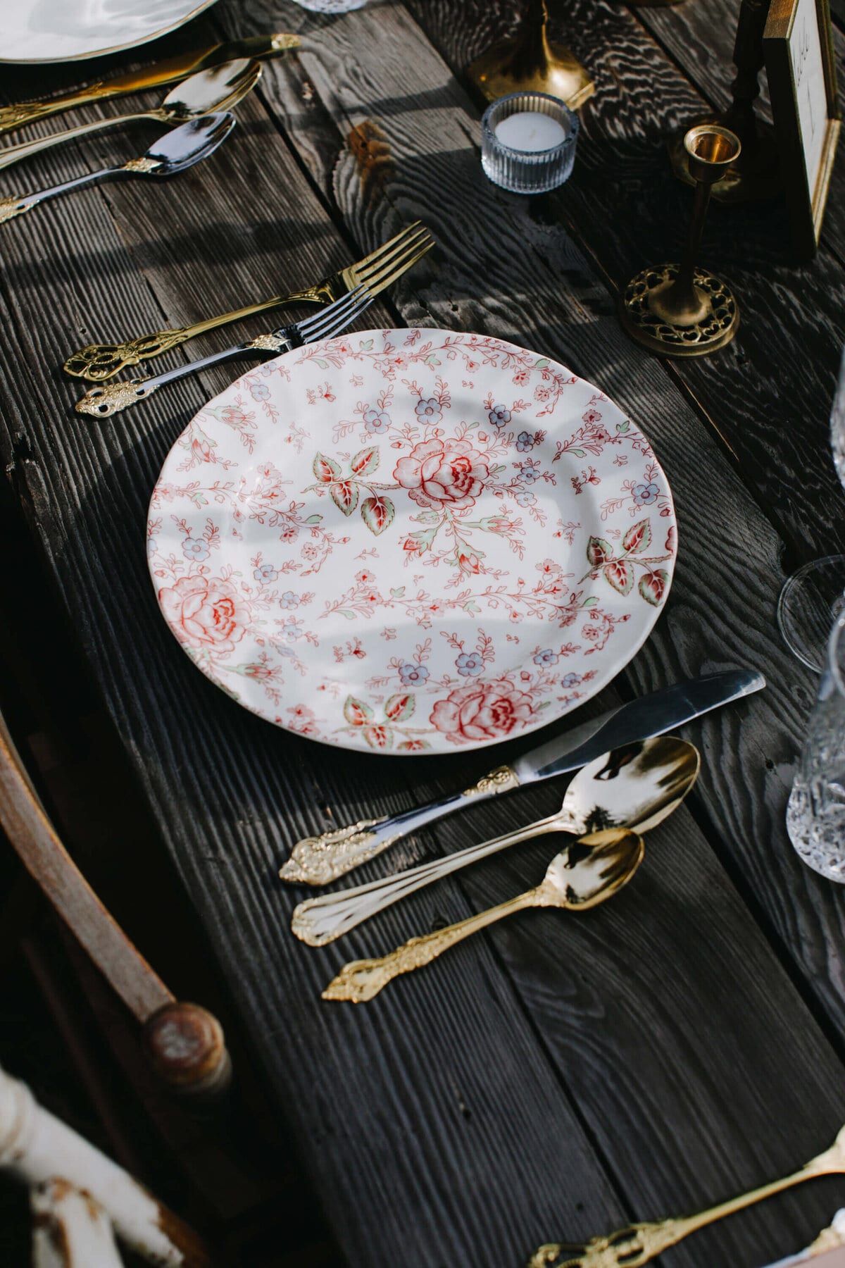 Rose chintz plate with gold flatware on dark planks