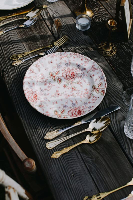 Rose chintz plate with gold flatware on dark planks