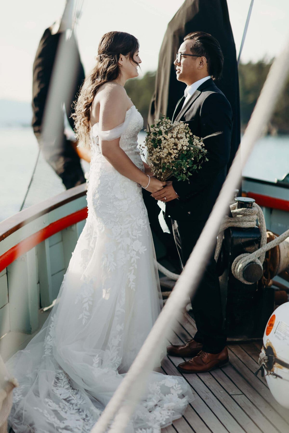 Bride and groom facing each other on deck, baby's-breath bouquet between them
