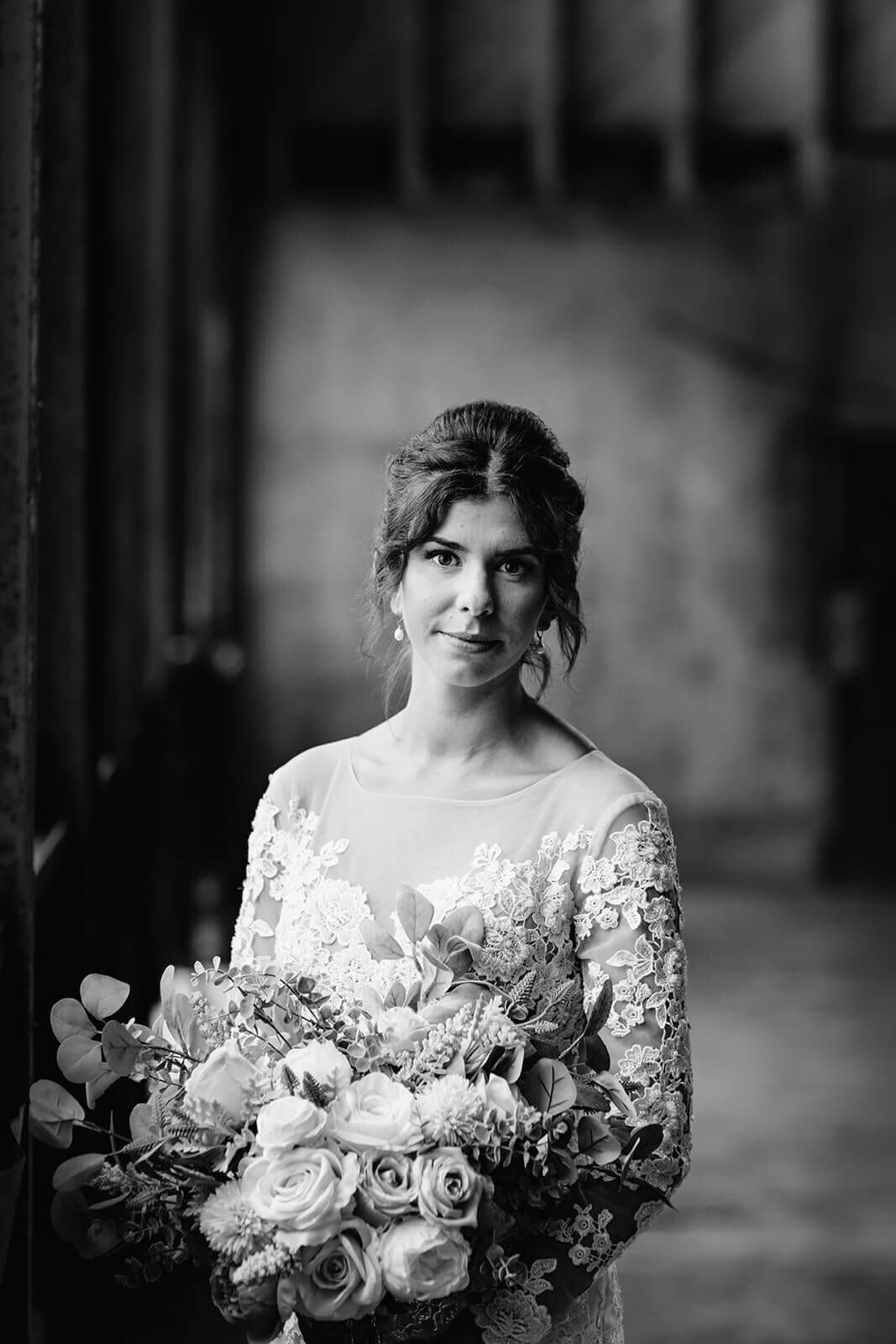 Black-and-white bride cradling roses in an industrial doorway