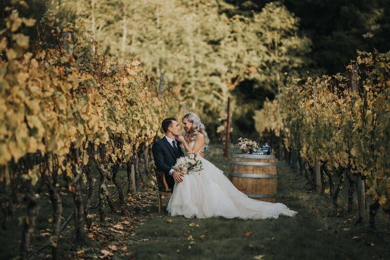Couple stealing a kiss between autumn vines at Deep Cove Winery