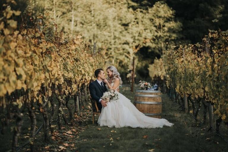 Couple stealing a kiss between autumn vines at Deep Cove Winery