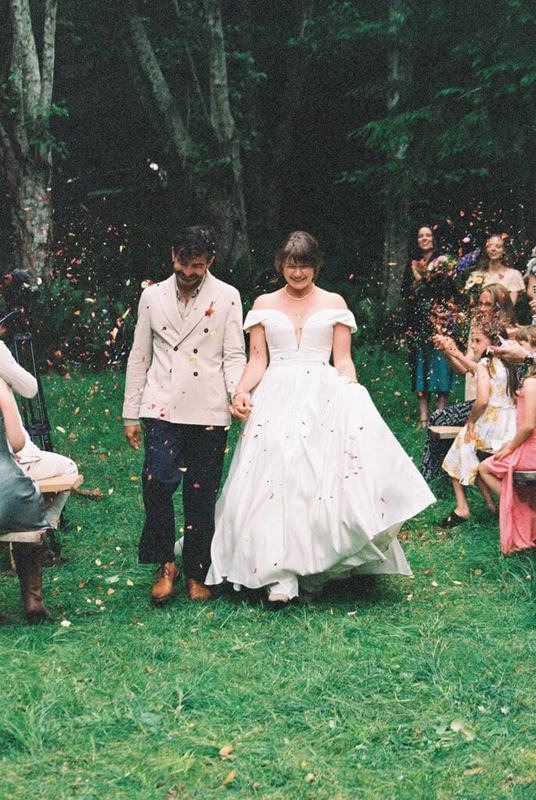 Couple walking the grassy aisle through tossed petals as guests cheer