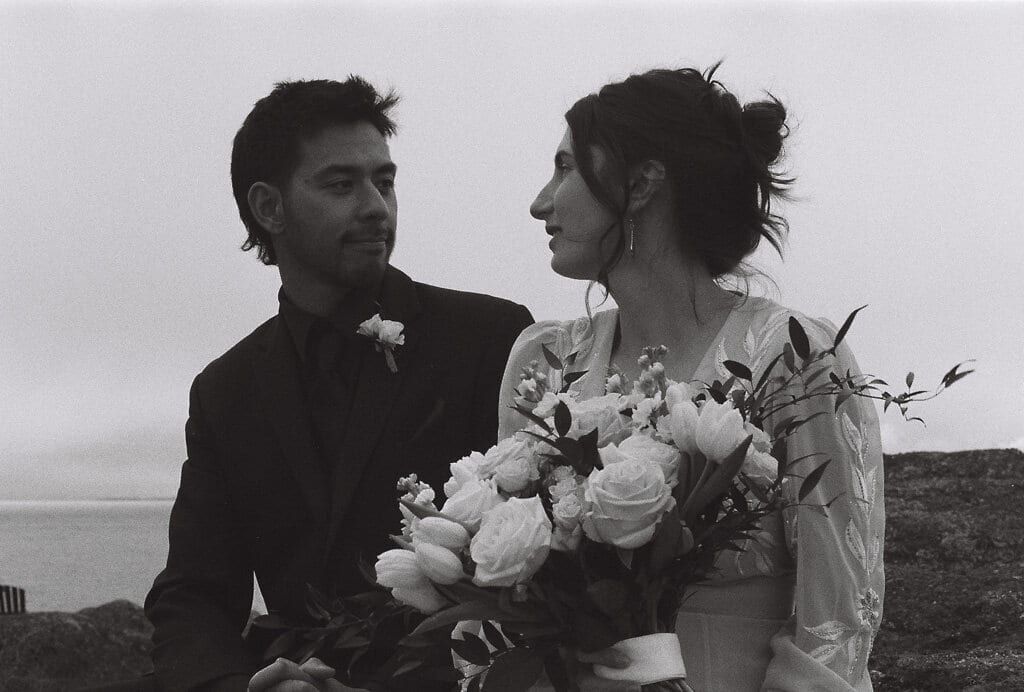 Bride gazing at her groom over a bouquet of roses by the sea