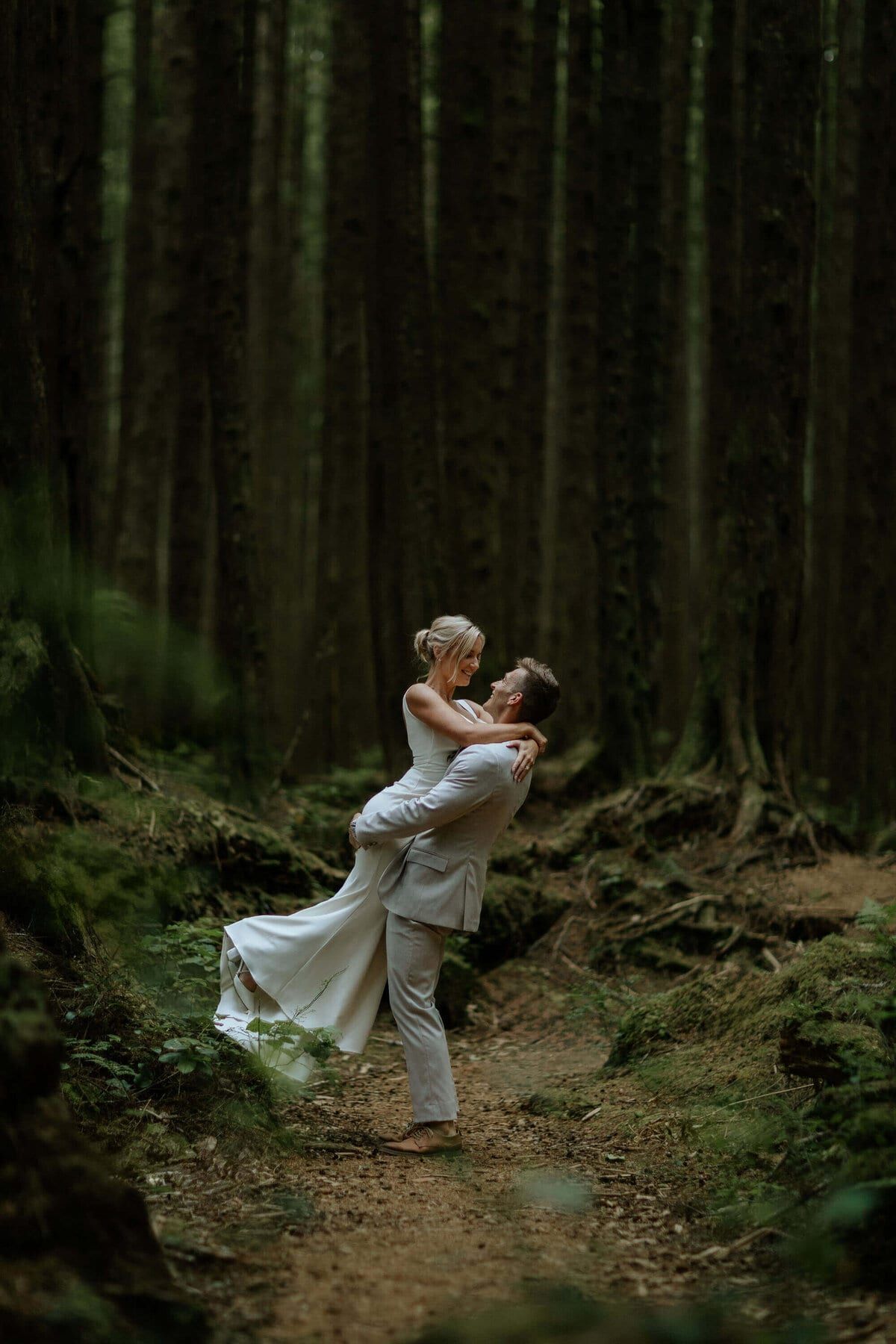 Groom lifting his bride off her feet on a forest trail