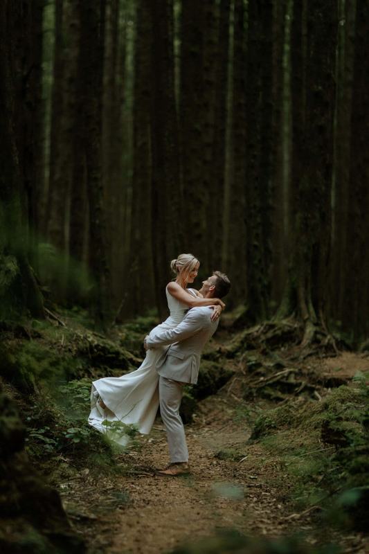 Groom lifting his bride off her feet on a forest trail