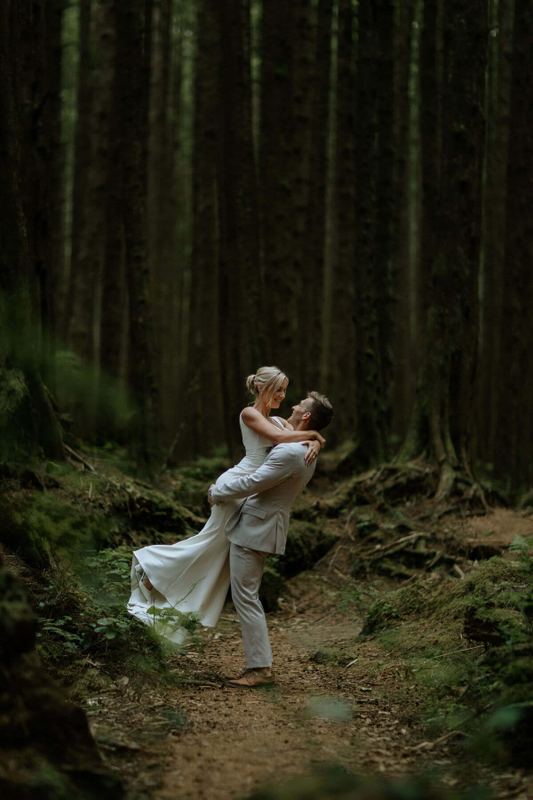 Groom lifting his bride off her feet on a forest trail