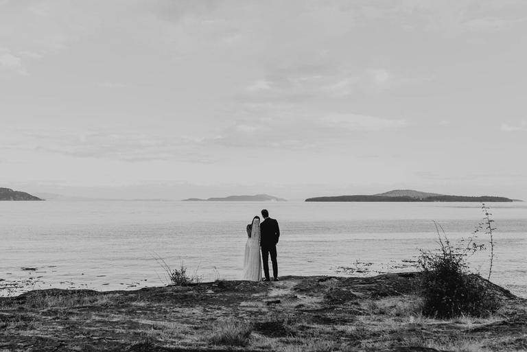 Couple gazing across calm water toward distant islands, black and white