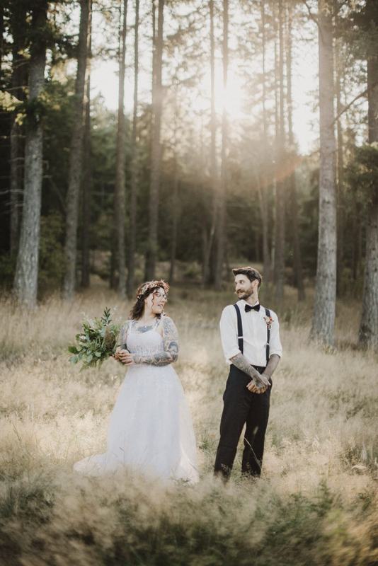 Flower-crowned bride and suspendered groom in a sunlit forest meadow