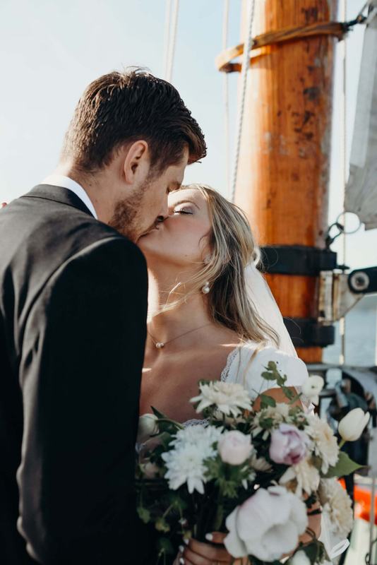 Newlyweds kissing beside the mast with a blush and white bouquet