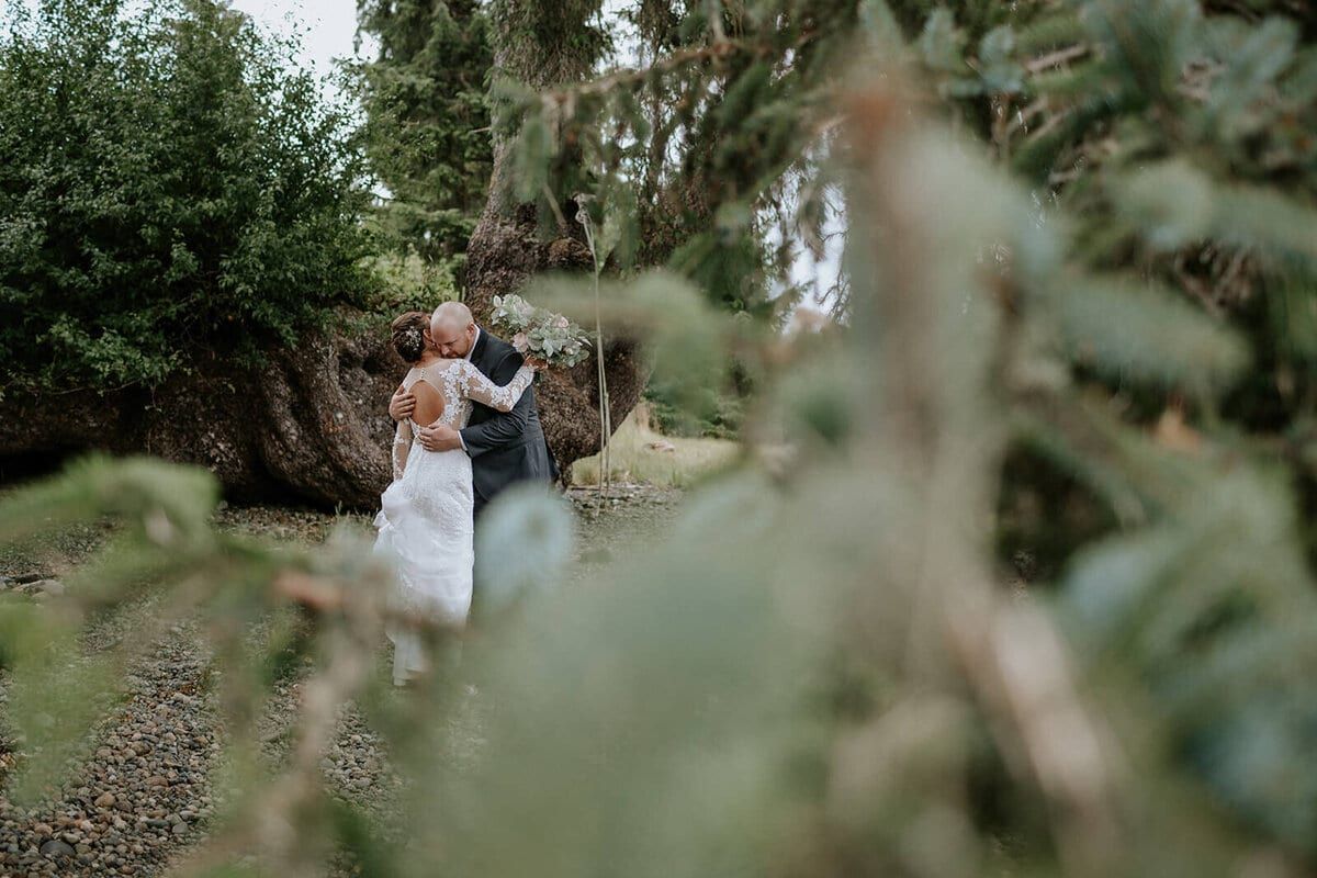 Couple embracing by mossy boulders, framed through evergreen branches