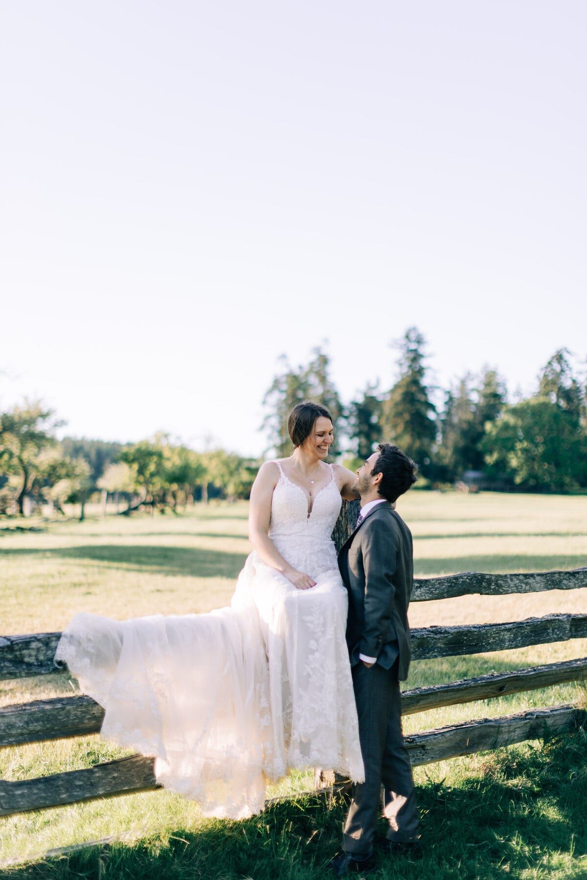 Bride smiling down at her groom from a fence rail