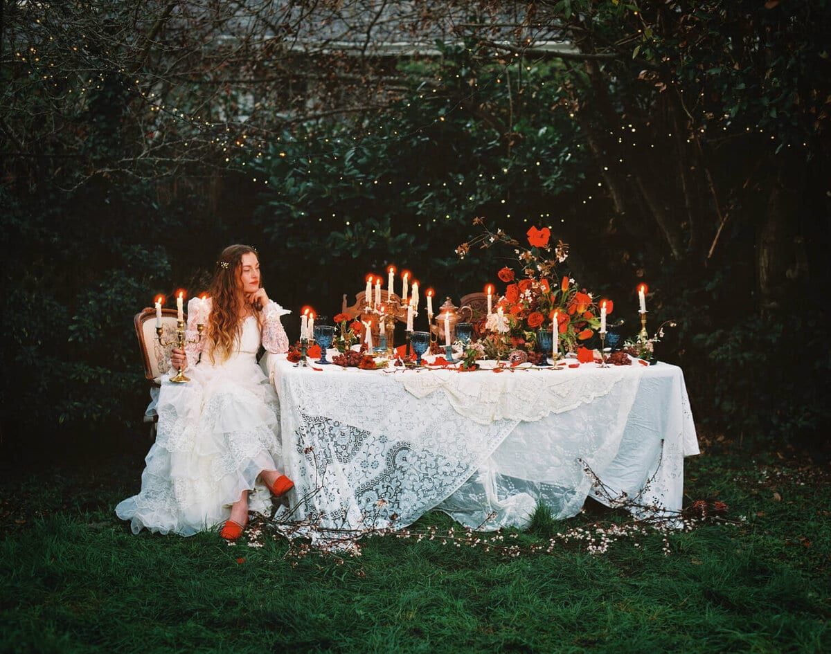 Bride seated at a candlelit garden table draped in lace