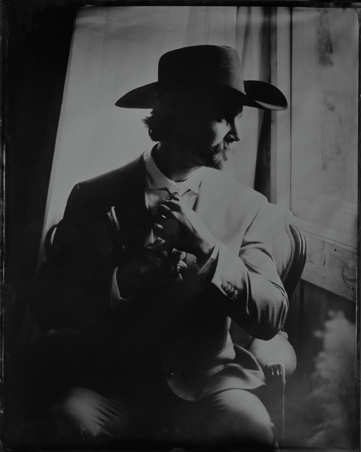 Moustached man in a cowboy hat lit dramatically beside a window