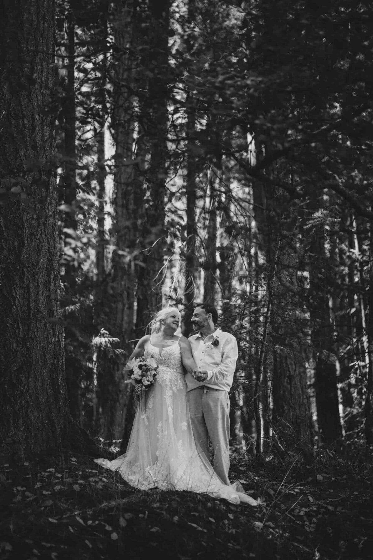 Newlyweds smiling among towering trees in black and white