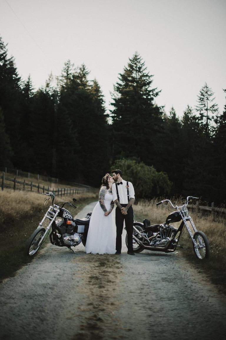 Bride and groom kissing between two choppers on a country road