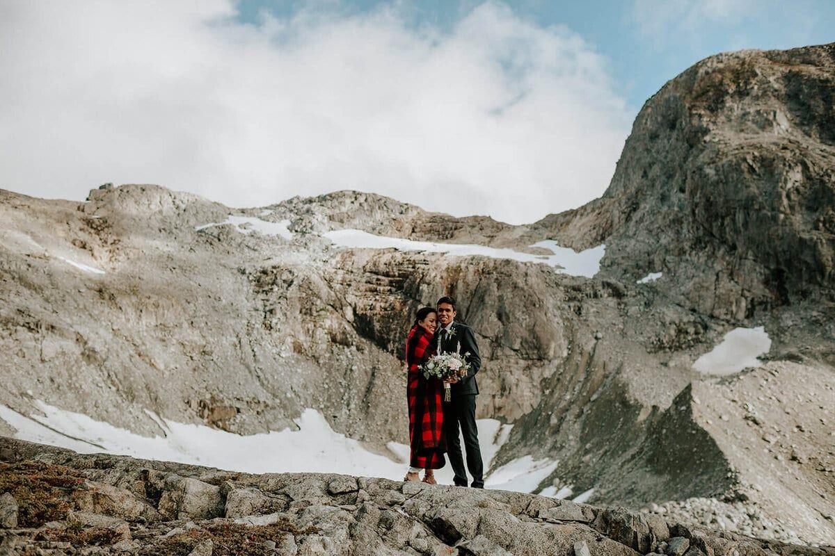 Couple wrapped in red plaid on a snow-patched alpine summit
