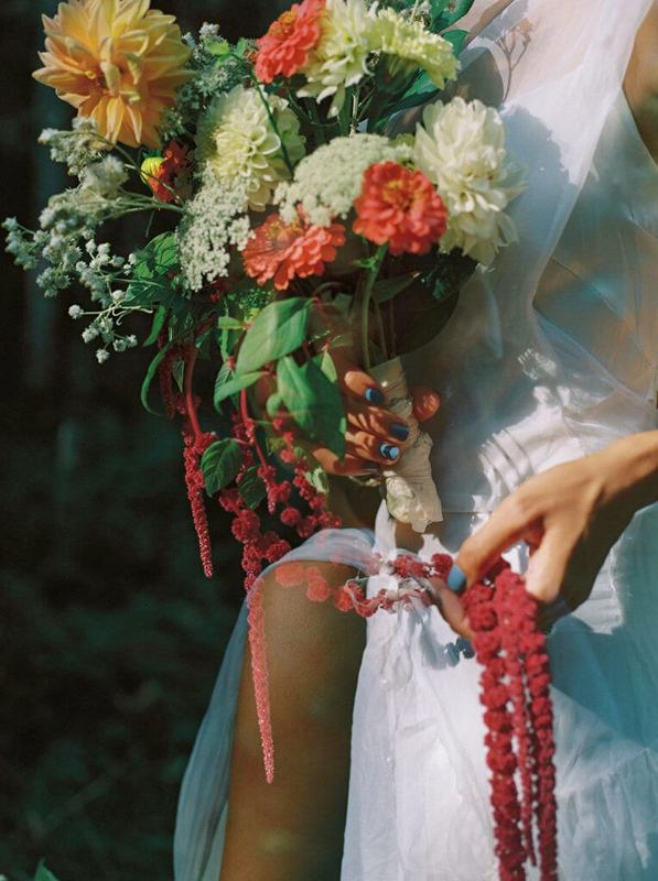 Colourful dahlia bouquet with trailing red amaranth held against a white dress
